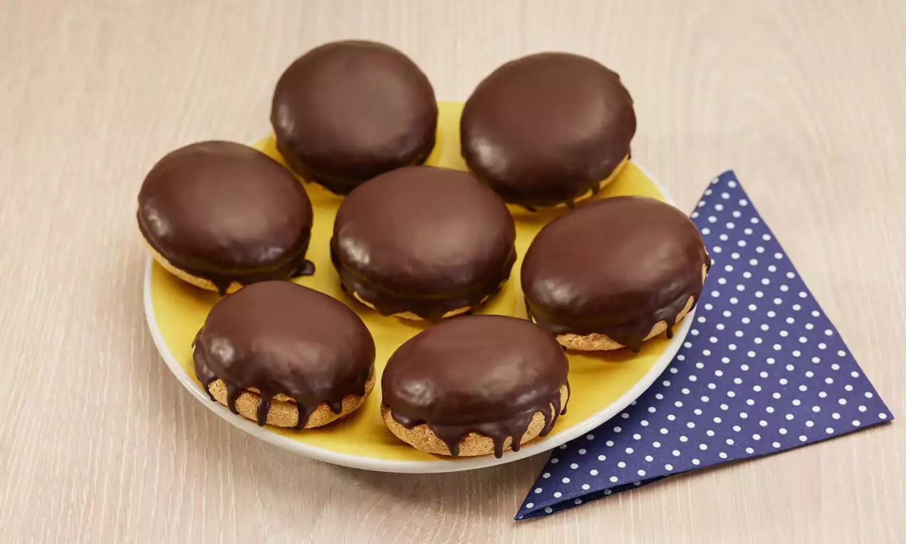 Petits dômes au chocolat brillant sur des bases biscuitées dorées, disposés sur une assiette jaune avec une serviette à pois bleu