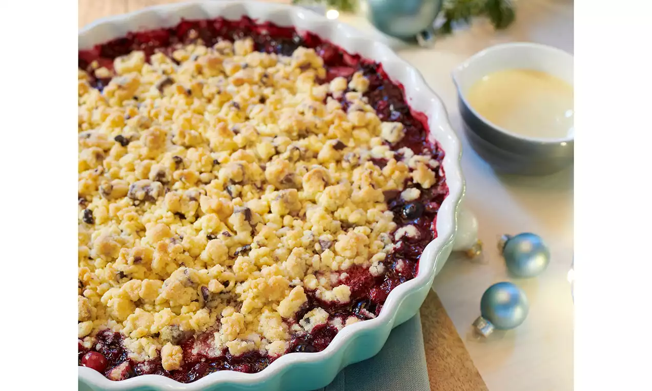 Božićni drobljenac s vinskim crvenim voćnim punjenjem prekriven zlatno smeđim prhkim mrvicama u valovitoj bijeloj keramičkoj posudi