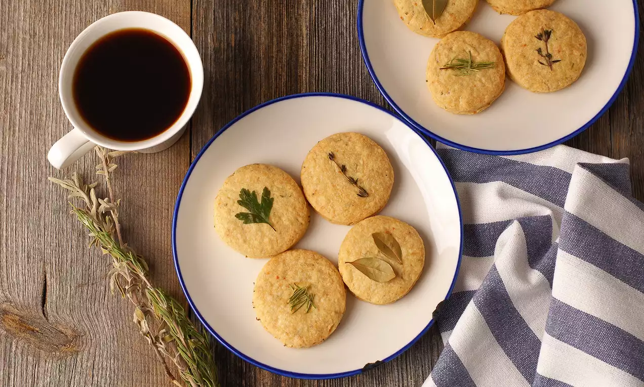 Altın rengi yuvarlak kurabiyeler üzerine yaprak ve baharat süslemesi, hoş bir şekilde düzenlenmiş tabaklar ve bir fincan kahve eşliğinde