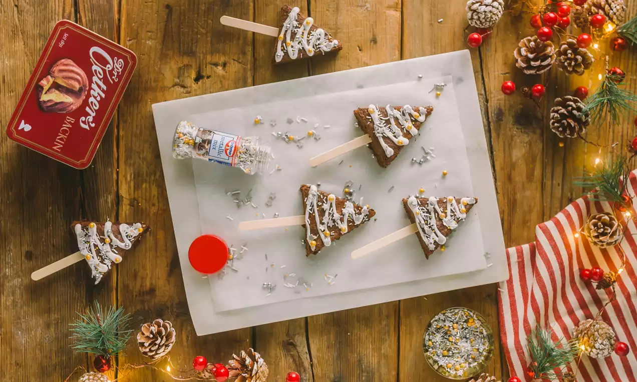 Arbolitos de navidad de bizcocho marrón con cubierta blanca de glaseado, decorados con confites brillantes sobre una mesa de madera