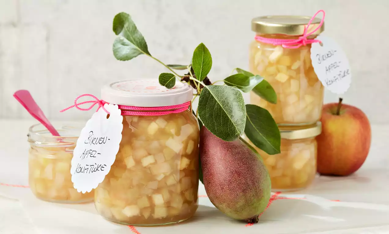 Barattoli di vetro trasparente colmi di dadini lucidi di pera e mela color oro, decorati con nastri rosa e etichette scritte a mano