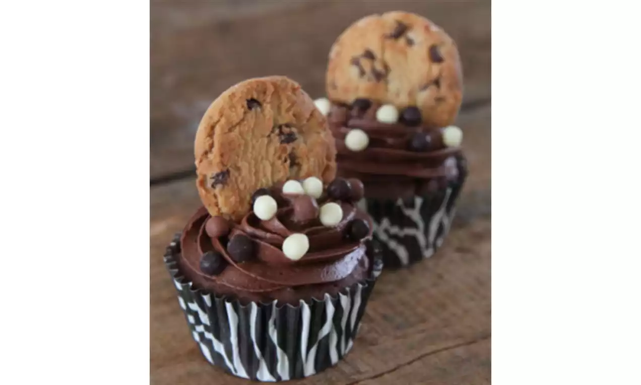 Cupcakes in zwart-wit vormpjes met een toef romige chocoladeglazuur, bolletjes decoratie en een lichtbruine chocolatechip-koek bovenop