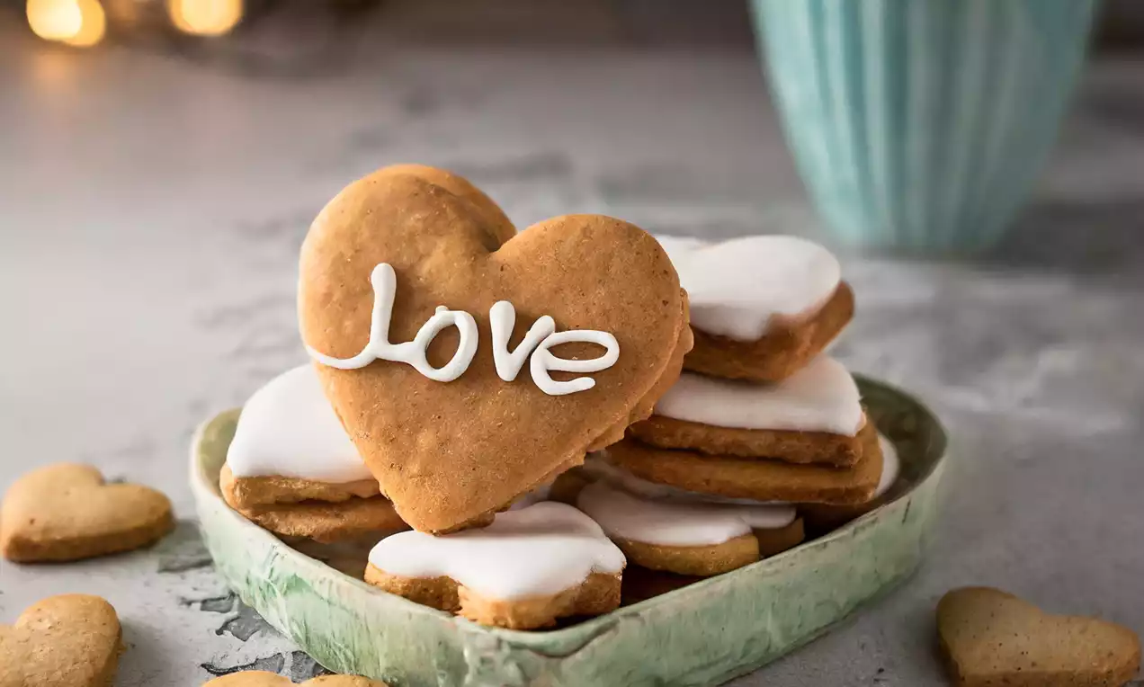 Biscuits dorés en forme de cœur, glacés de blanc, empilés sur un plat céramique vert avec une tasse turquoise en arrière-plan