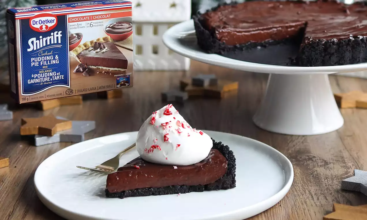 A slice of dark chocolate peppermint pie with a crumbly black cookie crust, topped with whipped cream and crushed peppermint on a white plate