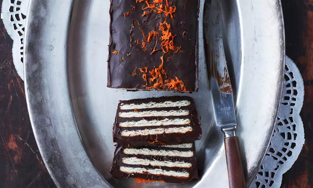 Rektangulær sjokoladetrekt kake med jevne lag av lys kjeks og krem, toppet med revet orange zest på et sølvfat med kniv