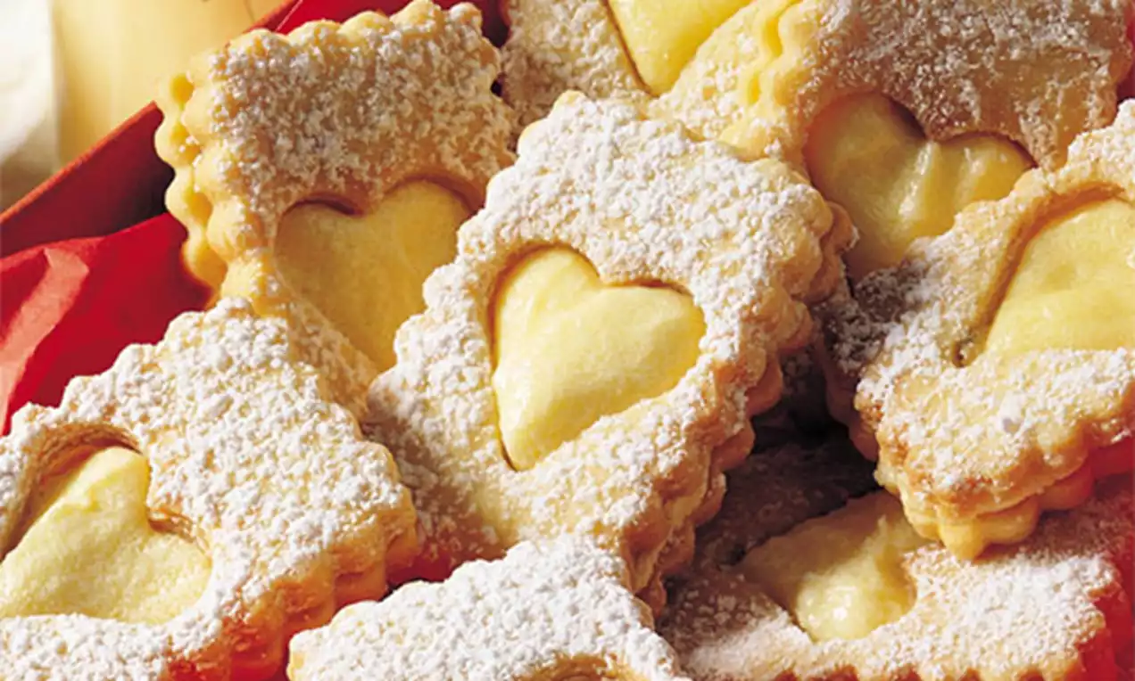 Vierkante eierlikeurkoekjes met gegolfde randen en een hartvormig venster, goudbruin en met poedersuiker bestrooid op een rode achtergrond