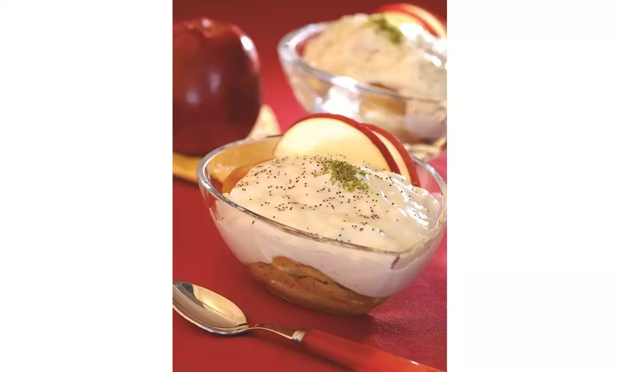 Şeffaf cam kaselerde servis edilen kremalı tatlının üzerinde dilimlenmiş kırmızı elmalar ve serpilmiş yeşil toz süsleme