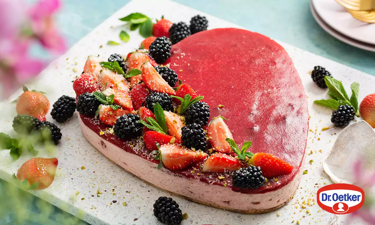 Srdcovitý dort s malinovo-růžovým krémem zdobený lesklým ovocným topem, čerstvými jahodami, ostružinami a lístky máty na keramickém podnosu