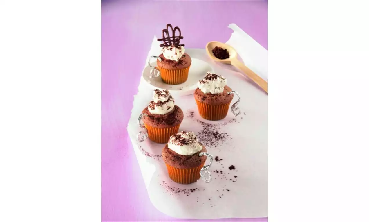 Chocolate muffins with a rich brown crumb, topped with fluffy white cream, chocolate shavings and arranged on parchment with a wooden spoon