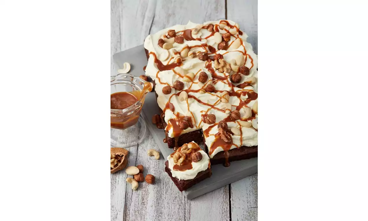 Saftige Brownies mit glatter Frischkäsecreme, karamellbrauner Soße und knackigen Nüssen auf einem grauen Teller angerichtet