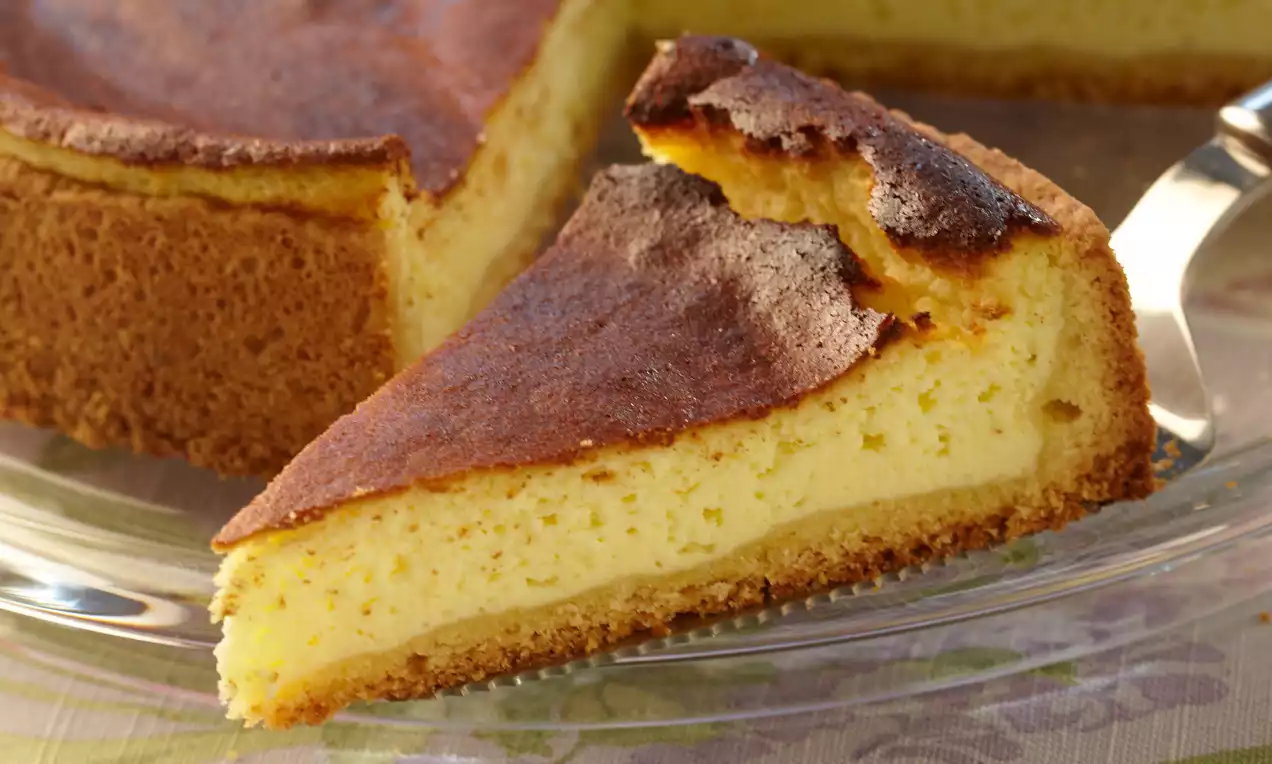 Gâteau au fromage doré avec une croûte épaisse brun clair, texture crémeuse, tranche coupée sur une assiette en verre transparente
