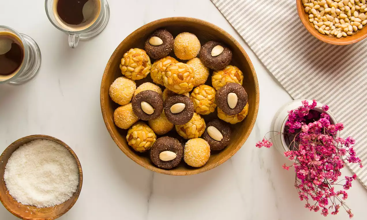 Panellets redondeados en tonos dorados, marrones y crema, con texturas de azúcar, frutos secos y cacao, dispuestos en cuenco de madera