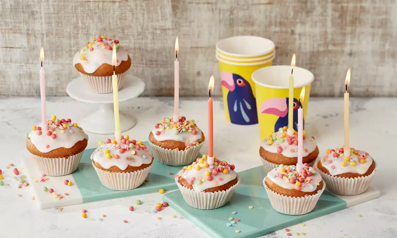 Fanta muffini s glazurom od bijelog šećera, šarenim mrvicama i zapaljenim svijećama, servirani na plavim podmetačima i stalku