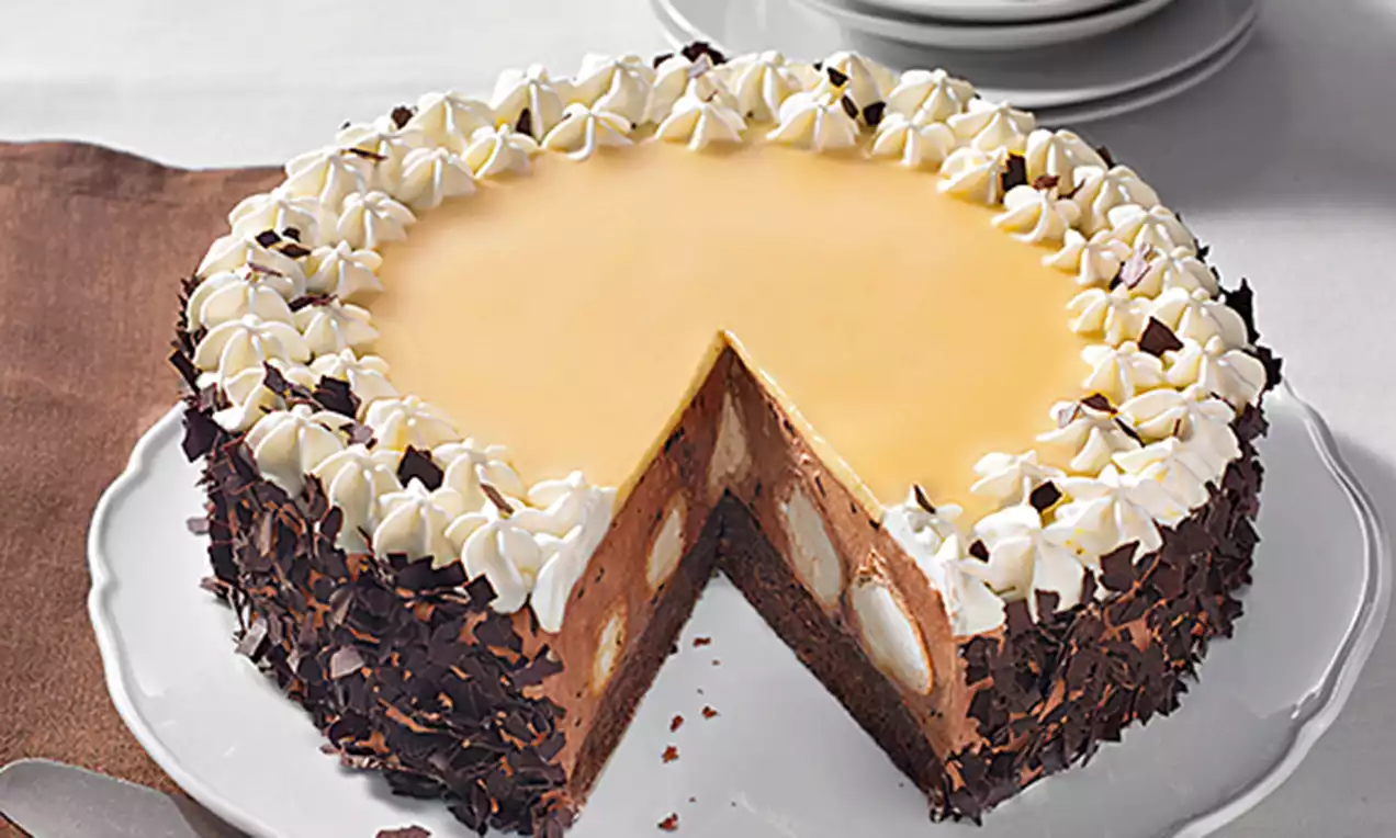 Runde Schokosahne-Torte mit glänzendem Karamellspiegel, Sahnetupfen, Schokoraspeln am Rand und sichtbaren Windbeuteln im Anschnitt