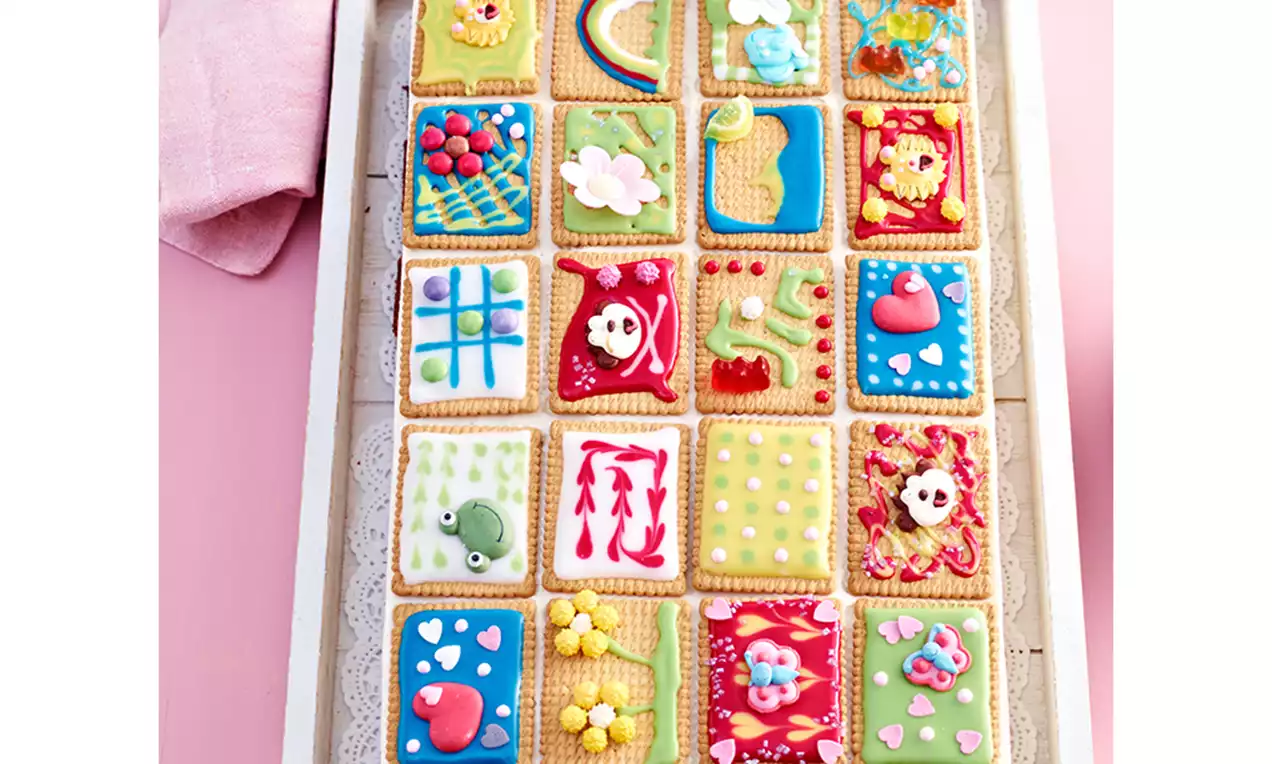 Butterkeks-Kuchen mit cremiger Vanillefüllung, Schlagsahne und kunterbunten verzierten Butterkeksen auf Teller