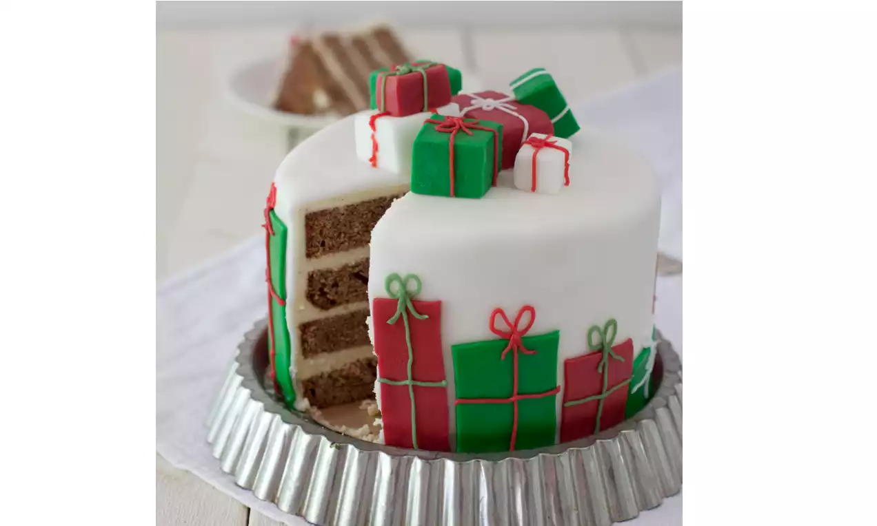 Vit, hög tårta med brunt inre, täckt av marsipanpaket i grönt och rött på topp och sidor, serverad på rund silverform