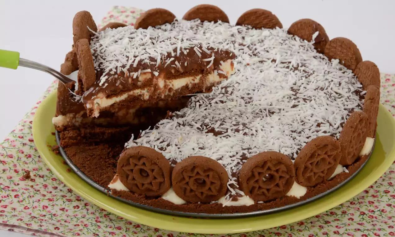 Torta de chocolate redonda com cobertura de coco ralado, decorada com biscoitos marrons nas bordas sobre um prato verde