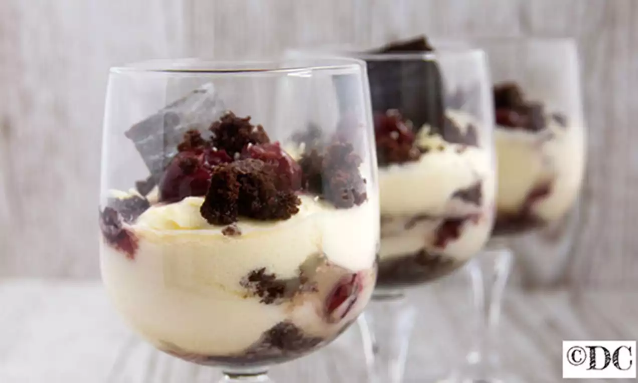 Luchtige mousse in glazen, met lagen van room, diep donkerbruine cakekruimels, glanzende rode kersen en stukjes chocolade