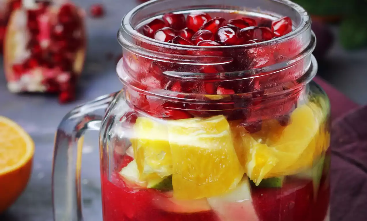 Glass jar layered with deep red smoothie, bright yellow and green fruit chunks, topped with glossy ruby-red pomegranate seeds