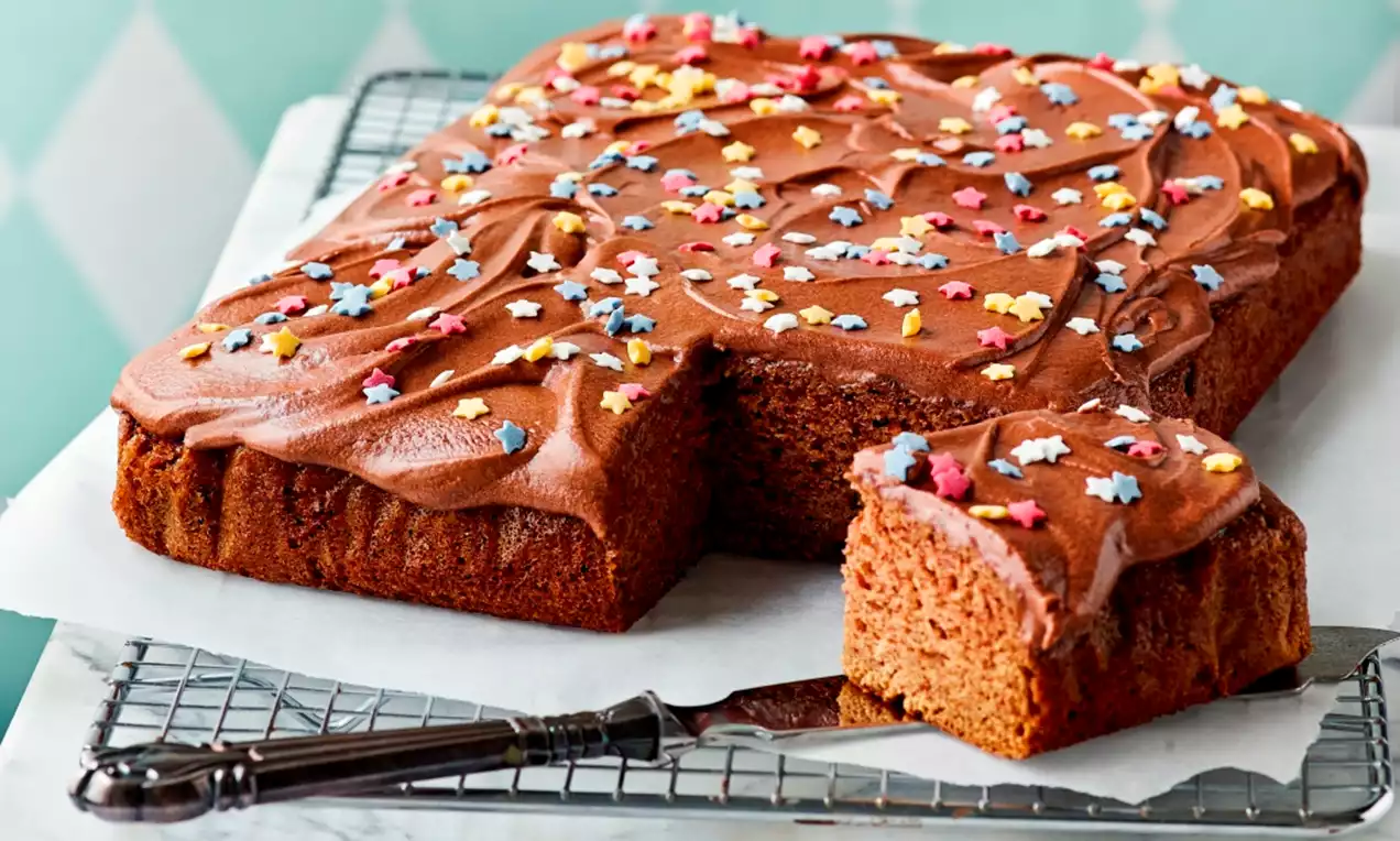 Nelikulmainen kanelikakku pehmeällä mokkakuorrutuksella, pinnalla värikkäitä tähtikoristeita, tarjolla metalliritilällä marmorialustalla