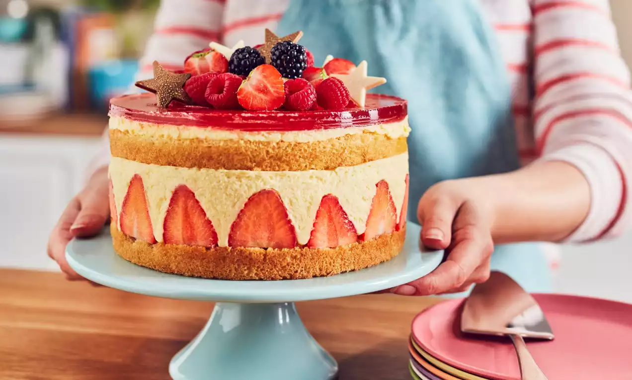 A Strawberry Fraisier Cake with golden sponge layers, pale cream filling, strawberry halves lining the sides, and berry-topped jelly glaze