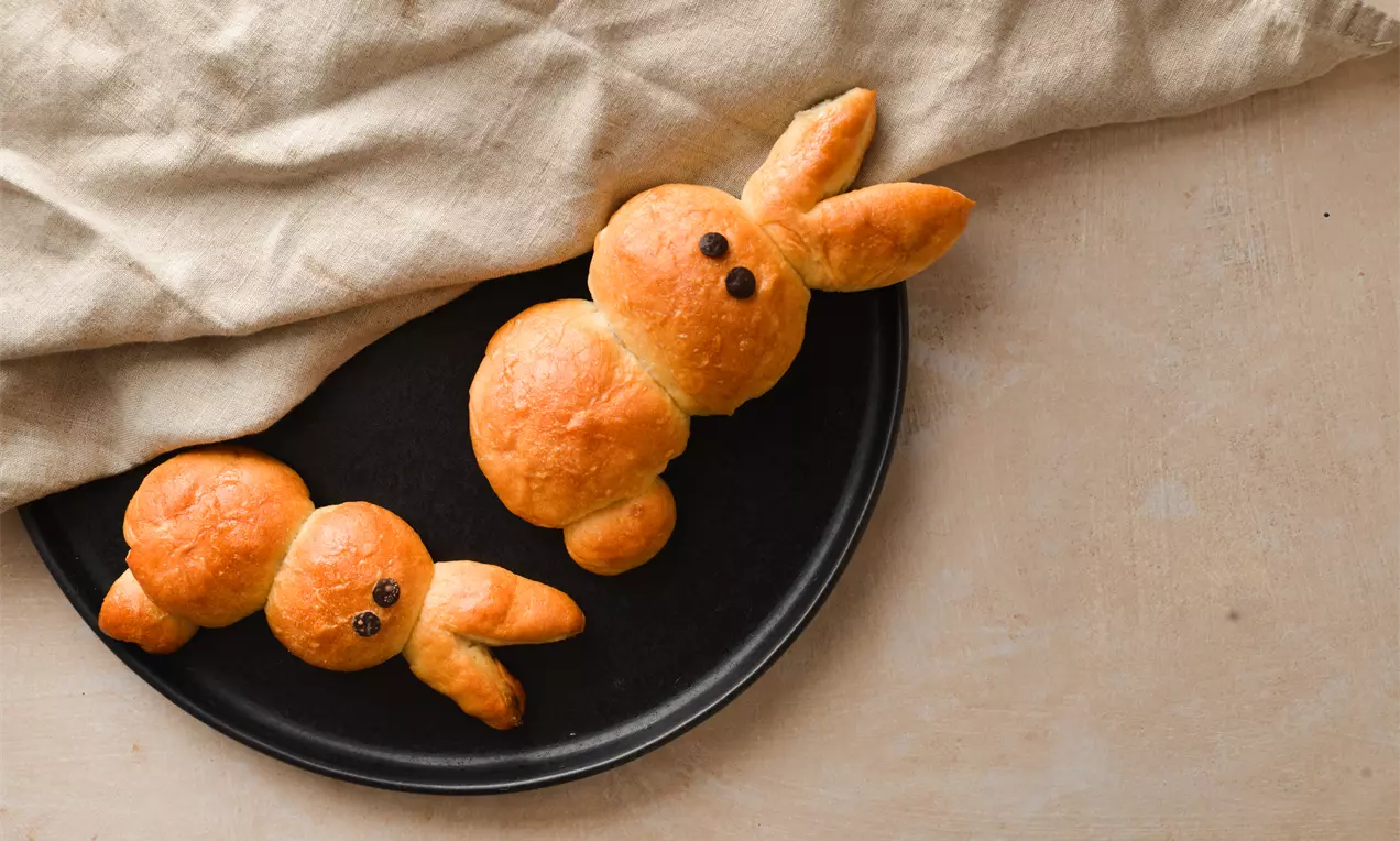 Златисто-кафяви, леко лъскави зайци с меко тесто, оформени с кръгли телца и остри уши, лежащи върху черна чиния до светъл ленен плат