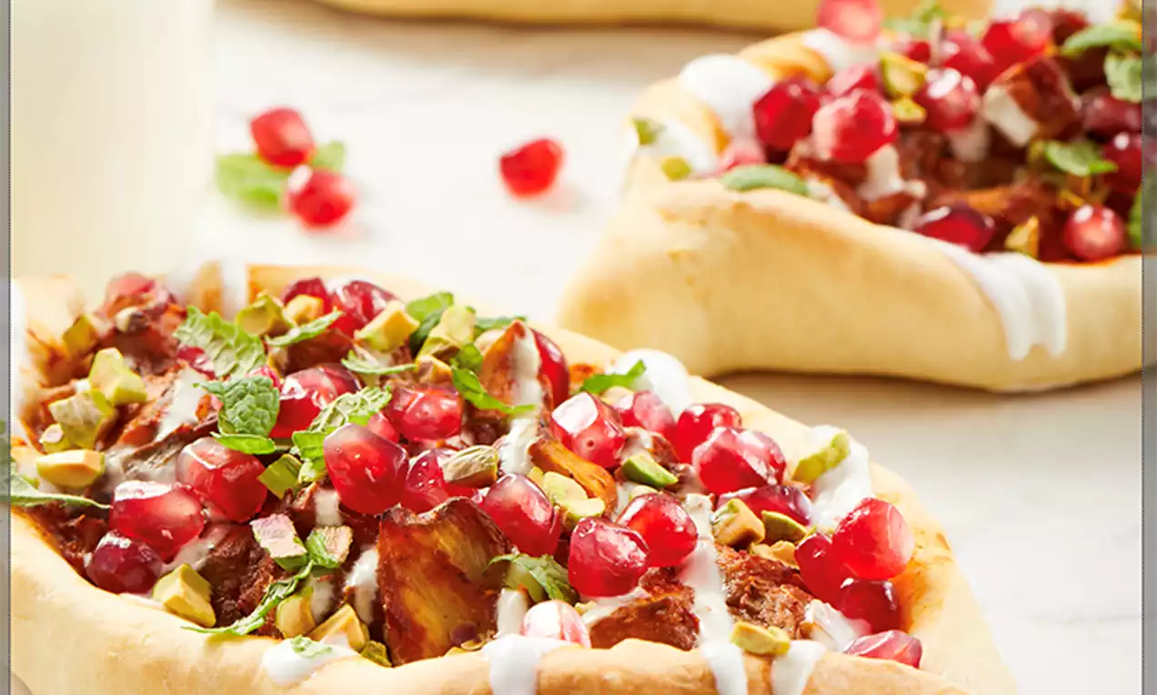 Boat-shaped golden-brown crusts filled with colorful pomegranate seeds, chopped pistachios, fresh herbs, and drizzled yogurt sauce