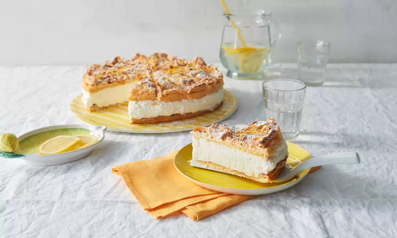 Zitronen-Baiser-Torte mit goldbrauner, knuspriger Baiser-Kruste auf einer gelben Platte und ein Stück auf einem gelben Teller mit Serviette