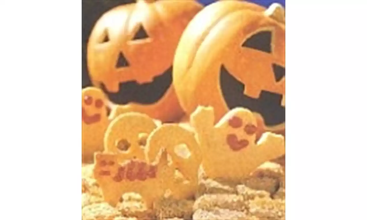 Biscuits sablés dorés en forme de fantômes et animaux avec décorations rouges sur lit de miettes devant des citrouilles sculptées