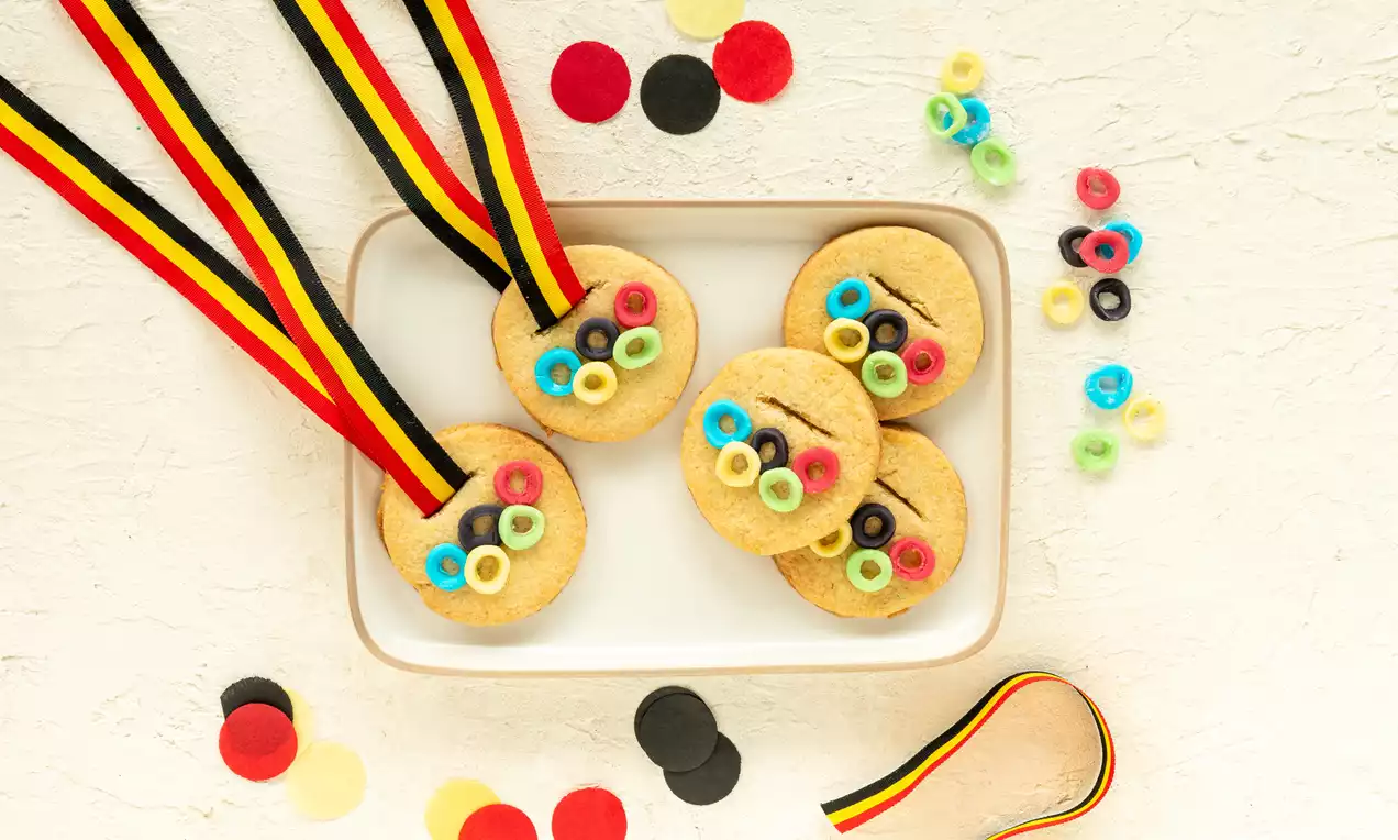 Biscuits dorés ronds décorés de cercles multicolores, ornés de rubans rouge, jaune et noir, disposés sur une assiette blanche