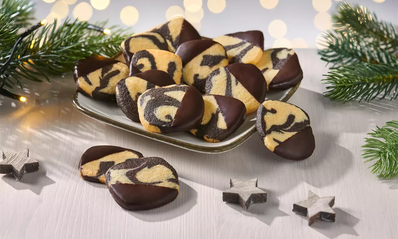 Altın sarısı ve kahverengi mermer desenli kurabiyeler, uçları çikolataya batırılmış, şık bir tabakta çam dalları ve yıldız süslerle çevrilmiş