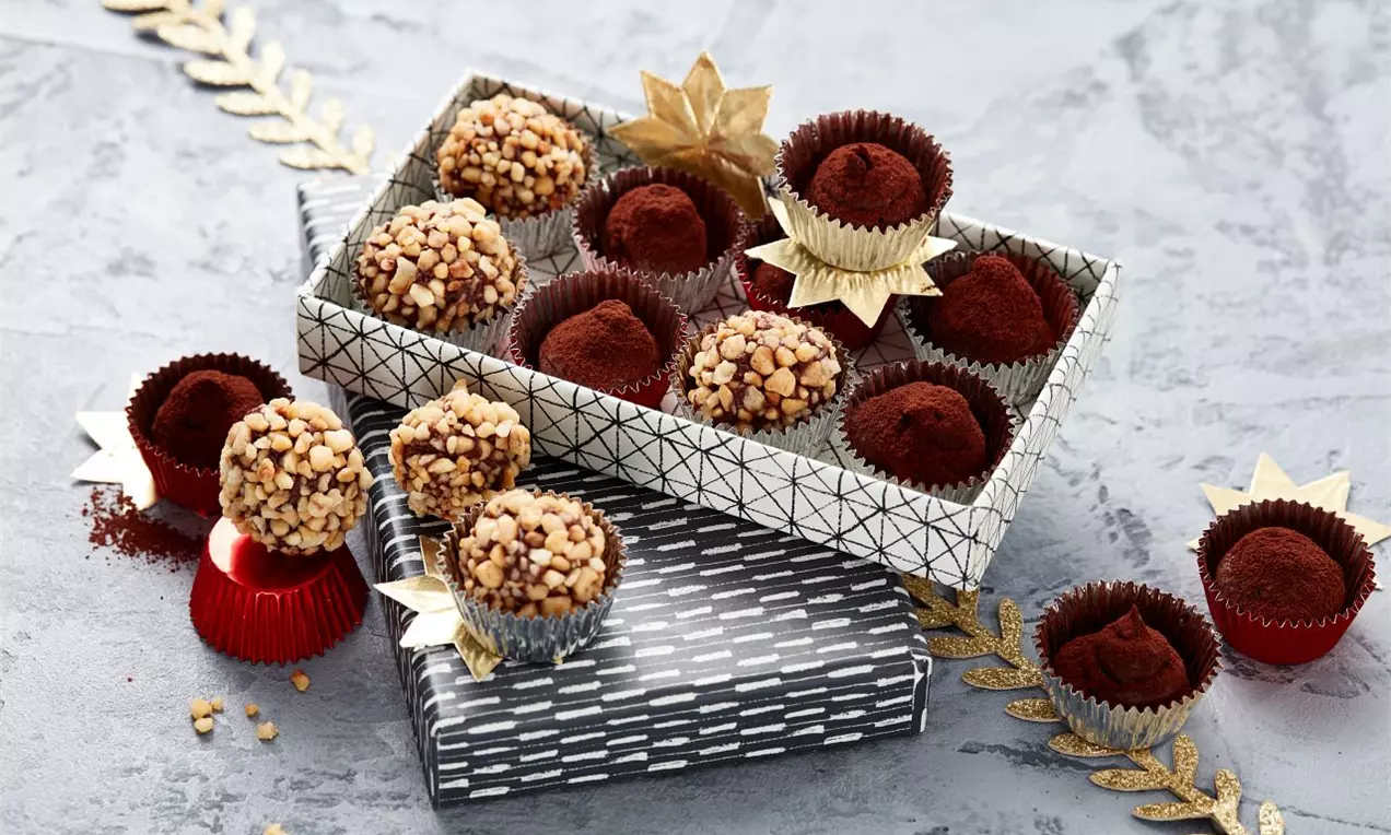 Krokantové čokoládové pralinky guľatého tvaru, posypané orechovou drťou alebo obalené v kakau, úhľadne uložené v ozdobných košíčkoch na striebornej krabici