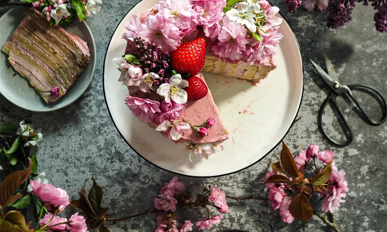 Вита торта с тънки слоеве блед меден пандишпан и крем маскарпоне, украсена с ягоди и нежни розови цветя върху бяла чиния