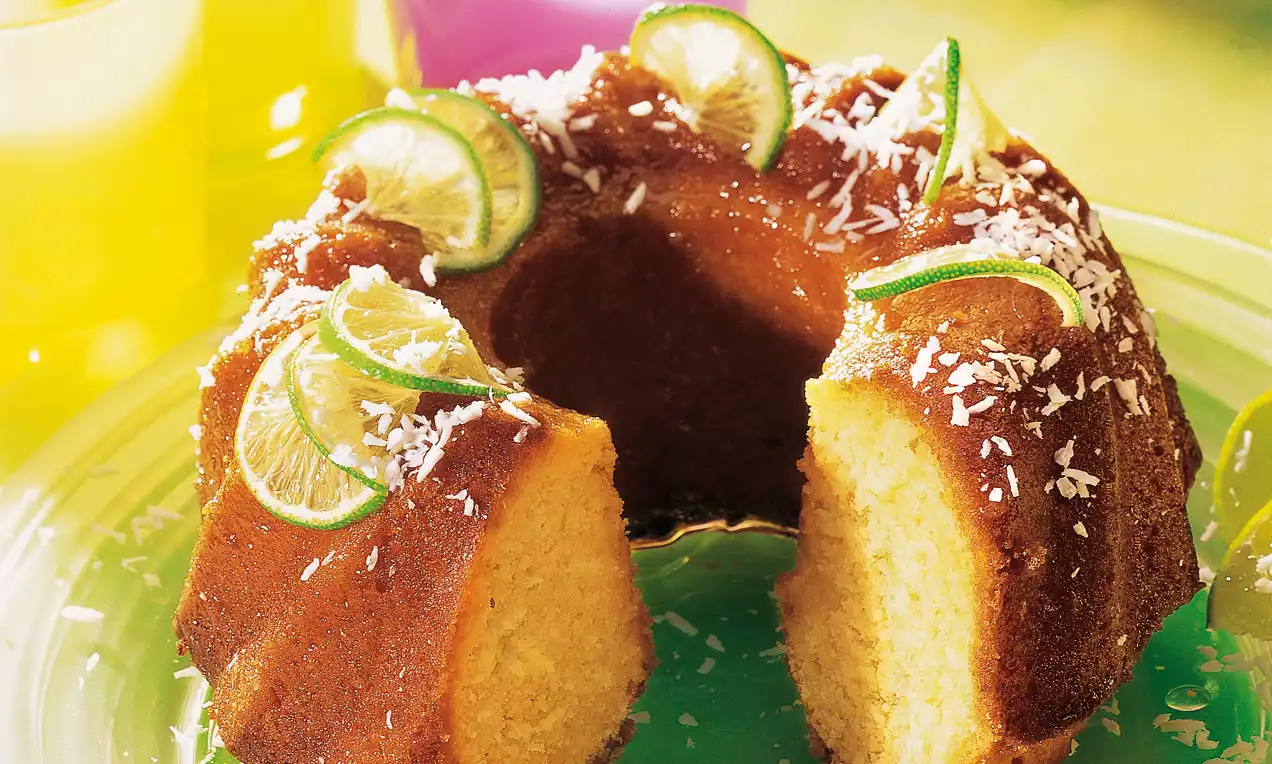 Gâteau moelleux en forme de couronne dorée, décoré de rondelles de citron vert et de copeaux de noix de coco sur une assiette transparente