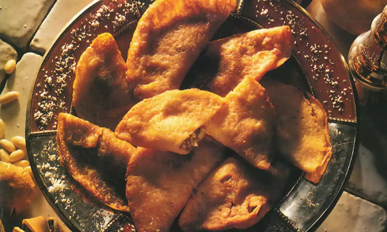 Goudbruin gefrituurde Turkse flensjes met licht gekrulde randen, rijkelijk bestrooid met poedersuiker op een glanzend schaal van glas