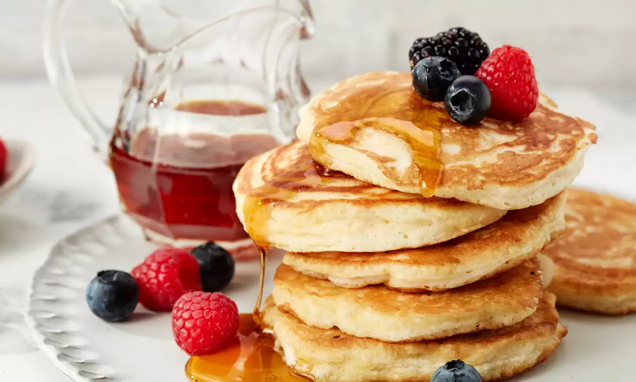 Goldbraune Pancakes in einem Stapel, mit glänzendem Sirup übergossen und frischen Himbeeren, Brombeeren und Blaubeeren dekoriert