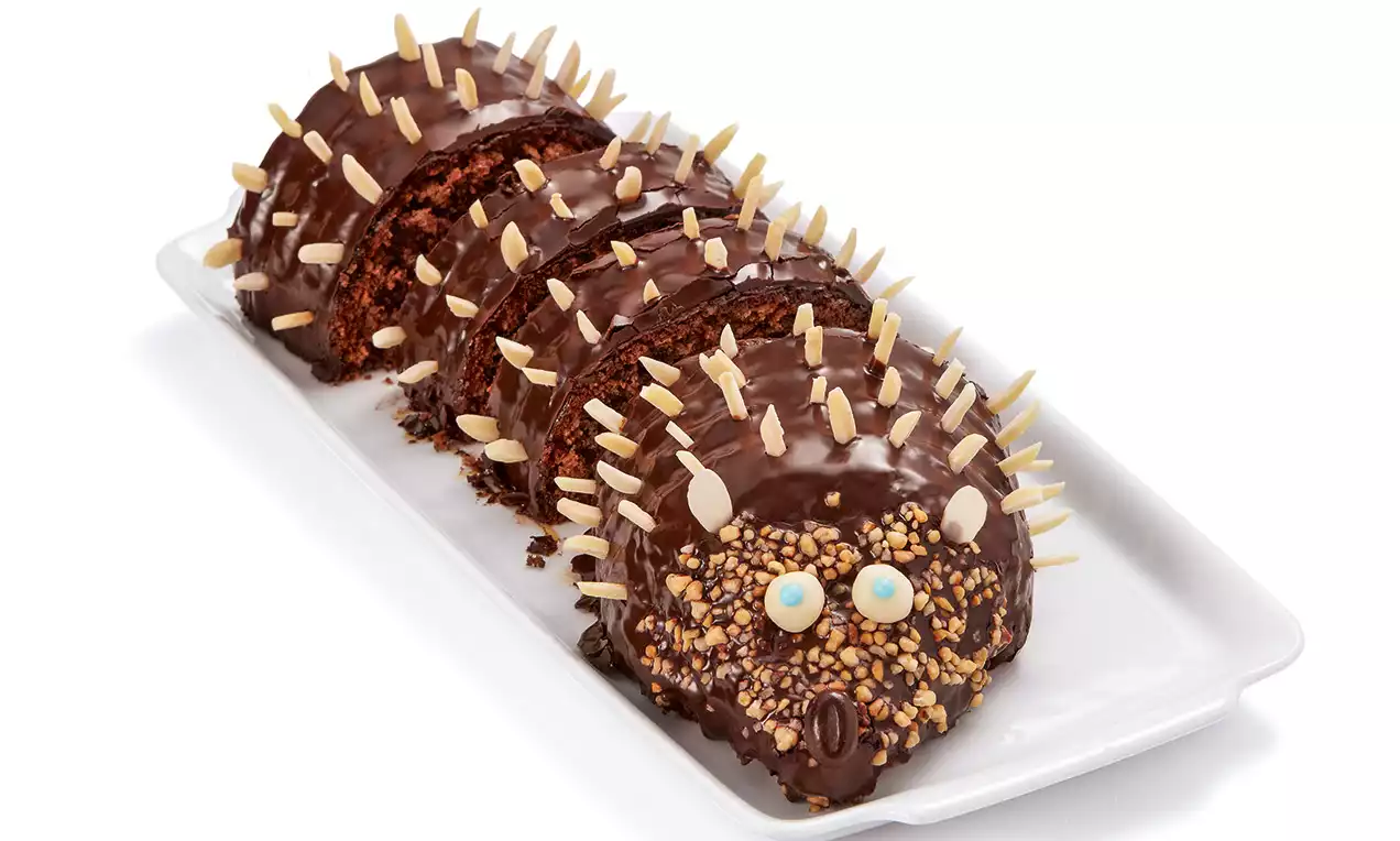 Gâteau en forme de hérisson avec glaçage chocolat brillant, éclats d'amandes en piques, billes sucrées pour les yeux sur un plat blanc