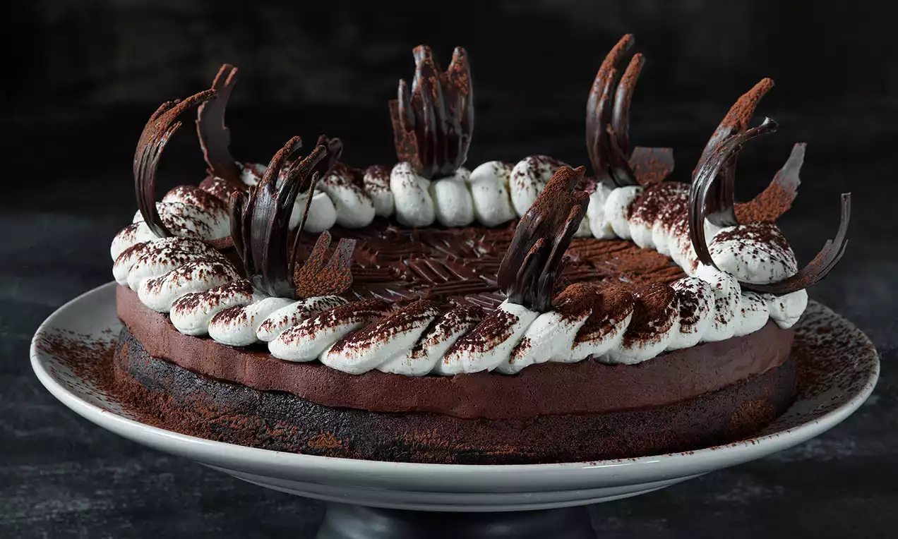Kruhový kakaový dort s bohatým čokoládovým povrchem, vrstvou šlehačky a dekoracemi z tmavé čokolády na bílém talíři