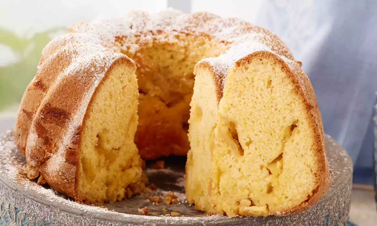 Gâteau Gugelhupf doré à la pâte moelleuse et garniture de pommes, saupoudré de sucre glace sur un plat rustique en pierre