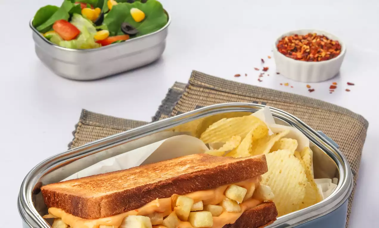Golden toasted sandwich with chunky, pale yellow fries inside, arranged with crisp potato chips in a light blue dish on a woven mat