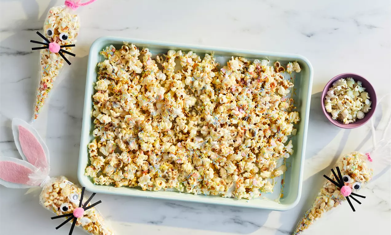 Rectangular mint-green tray filled with golden popcorn speckled with colourful sprinkles alongside cone-shaped bunny popcorn bags
