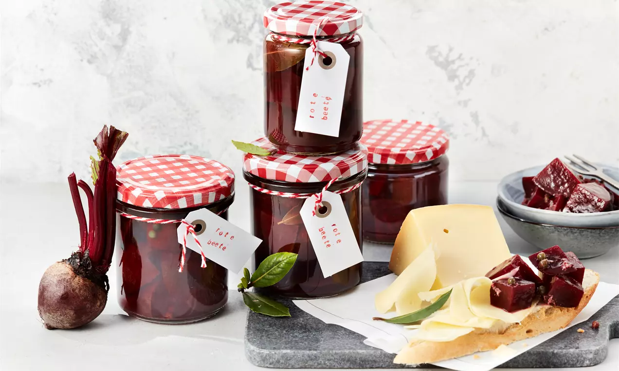 Staklenke s tamnocrvenom mariniranom ciklom, poklopci crveno-bijele karirane tkanine, etikete s oznakama, komadići cikle na tanjiru