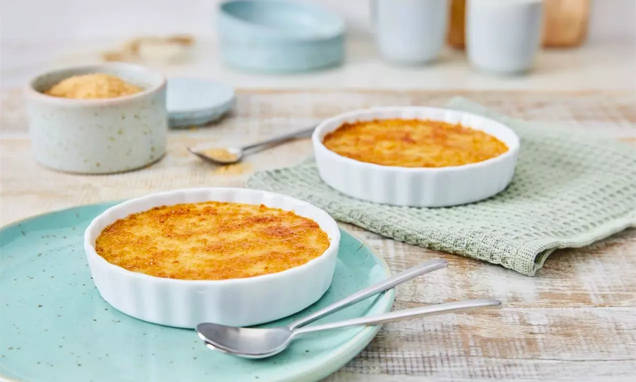 Златисто-кафява хрупкава коричка върху гладък крем в бели кръгли форми, сервирани на пастелни чинии с метални лъжици