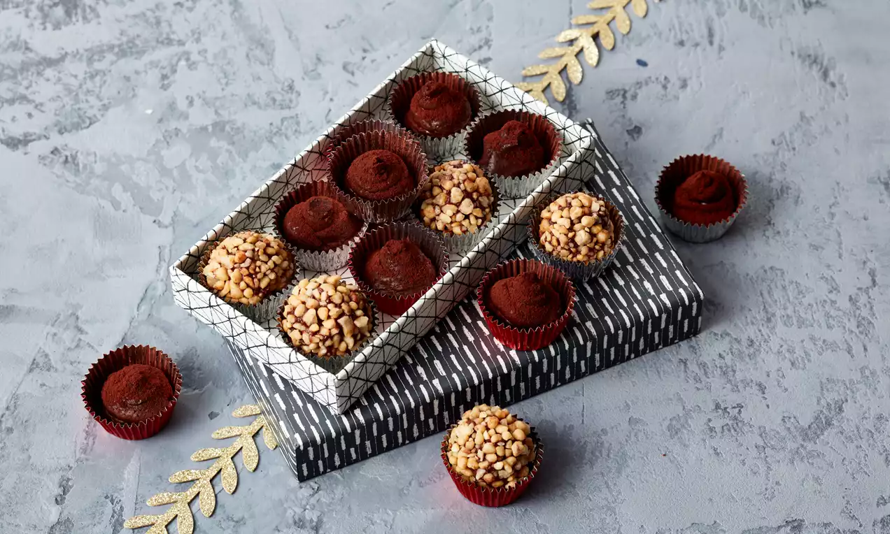 Truffes rondes au chocolat saupoudrées de cacao ou enrobées de noisettes concassées dans une boîte rayée sur fond texturé gris