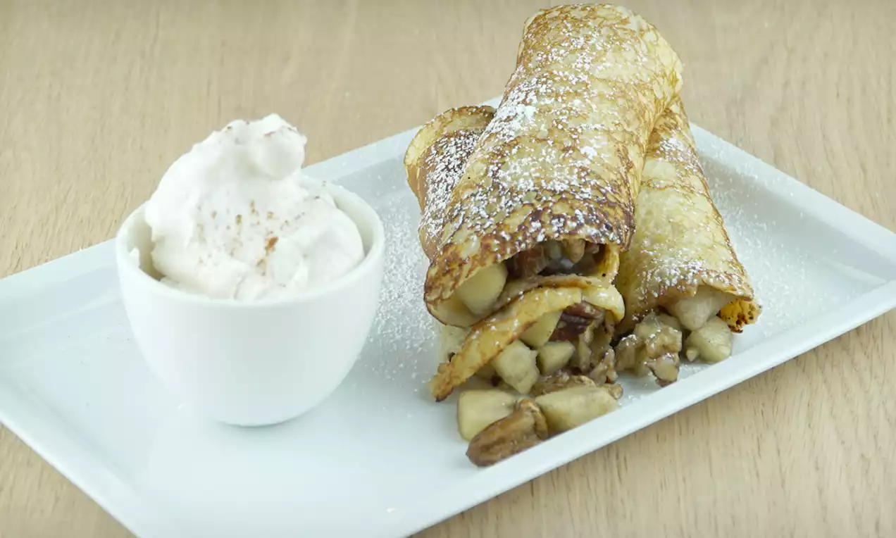 Dunne goudbruine pannenkoeken gevuld met stukjes appel en noten, licht bestrooid met poedersuiker, geserveerd naast een kom roomijs