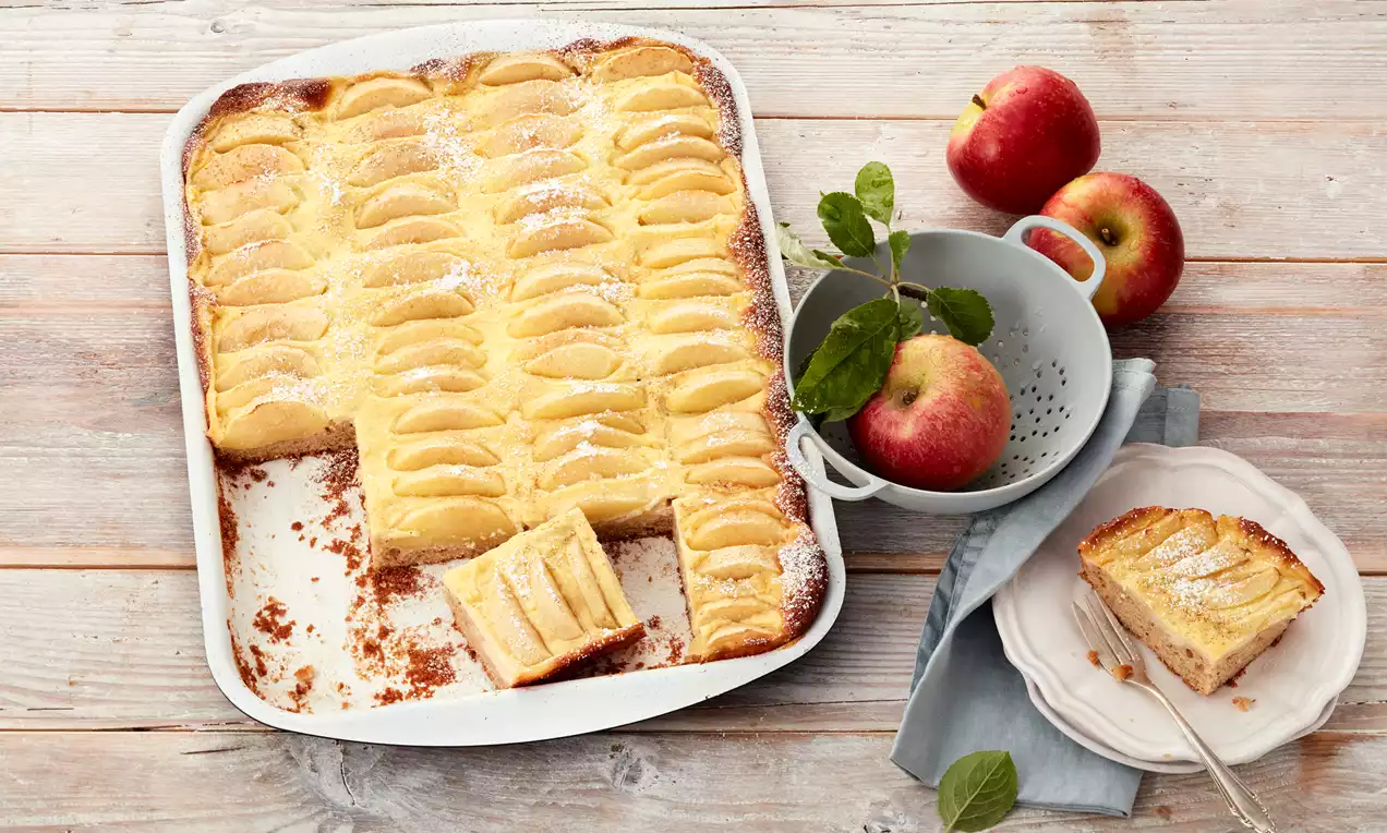 Apfel-Blechkuchen mit goldgelber Oberfläche aus fächerförmig angeordneten Apfelscheiben, bestäubt mit Puderzucker auf rustikalem Holztisch