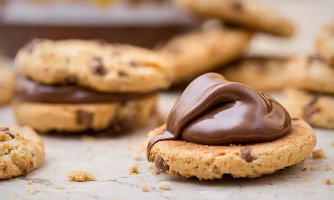 Knapperige ronde koekjes met chocoladestukjes, gegarneerd met een smeuïge toef gladde, glanzende Nutella op een licht oppervlak