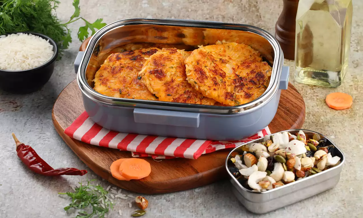 Golden-brown rice and vegetable pancakes with crisp edges stacked in a blue dish on a wooden board with scattered fresh ingredients
