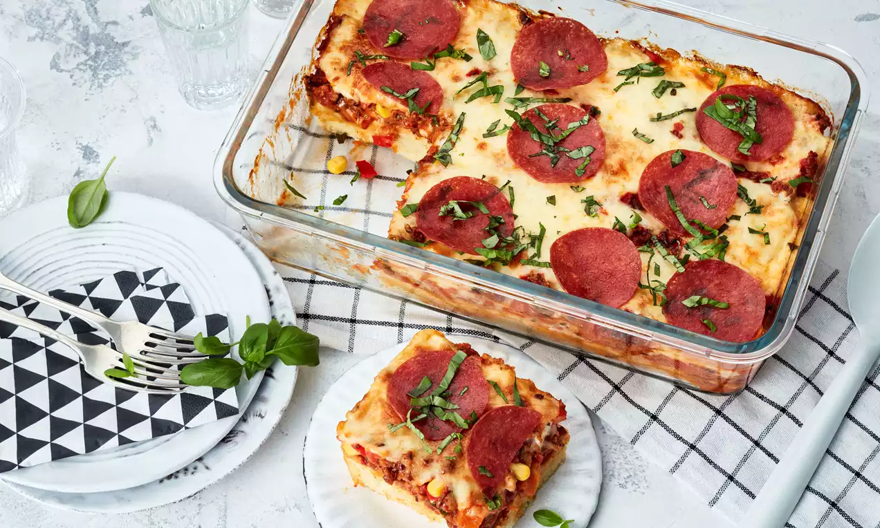 Pizza-Auflauf mit goldbrauner Käsekruste, Mozzarella, Tomatenscheiben, grünem Basilikum und knusprigem Teigrand