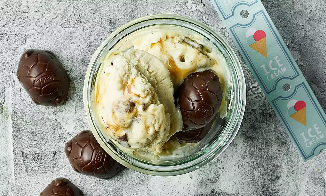 Vaniljegul is med karamelhvirvler i glaskrukke omgivet af blanke chokoladeskildpadder med rillet overflade på grå bordplade